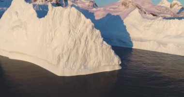 Günbatımında Antarktika sularında yüzen dev buzdağı, hava aracı görüntüleri. Antarktika buzul duvarının nefes kesici manzarası, arka planda dağlar. Sinematik ekoloji sahnesi. Panoramayı büyüt