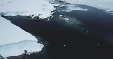 Antarktika 'daki kayalık kıyı şeridi karla kaplıydı. Soğuk sularda kayalar, arka planda dağlar olan donmuş kutup okyanus körfezi. Antarktika seyahati ve keşfi. Hava aracı görüntüsü