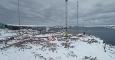 Antarktika 'daki kutup istasyonunda insan telekom kulesi anteni onarımı. Telekomünikasyon mühendisi bakım hücresi sinyali. Arka planda Antarktika vahşi doğa okyanus kıyıları. İHA uçuşunu yakınlaştır