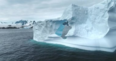 Antarktika manzarası. Erimiş delikli büyük buzdağı. Kutup okyanusu sürükleniyor. Kar arka planda dağları kapladı. Kış doğası. Ekoloji, eriyen buz, iklim değişikliği ve küresel ısınma kavramı