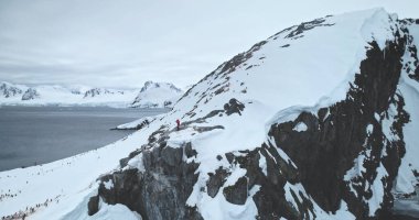 Turist yürüyüşü Antarktika vahşi doğasını keşfeder. İnsanlar dağdaki kayalıkların tepesinde durup penguenlerin ve buzulların fotoğraflarını çekiyorlar. Güney Kutbu güzelliğini keşfedin. Hava aracı panoraması
