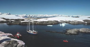 İnsanlar yatla Antarktika 'ya seyahat ediyor. Güney Kutbu 'nu keşfet. Kırmızı botta seyahat eden turistler kutup okyanusunda karla kaplı dağlarla vahşi doğa manzarasının tadını çıkarıyorlar. Turizm gezileri. Hava aracı görüntüsü