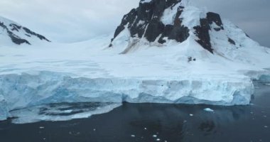 Muazzam mavi buzullar Antarktika 'nın kutup buzullarını kaplıyor. Dağlar karla kaplı kıyı şeridi. Ekoloji, eriyen buz, iklim değişikliği küresel ısınma. Antarktika vahşi doğa manzarasını keşfedin. İHA uçuşu