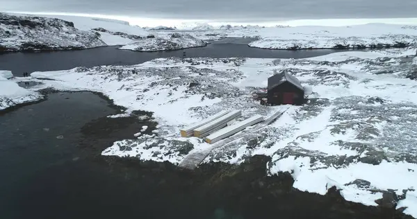 Antarktika kayalık kıyılarında yapayalnız bir bina, karla kaplı ada körfezi, arka planda dağlar. Karlı araziyle çevrili kutup istasyonunun hava görüntüsü. Güney Kutbu 'na yolculuk.