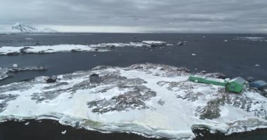 Antarktika 'nın kayalık adasındaki kutup istasyonu binaları. Donmuş sahil, soğuk okyanus, arka planda dağlar. Kış vahşi doğa manzarası. Antarktika seferleri, seyahatler. Güney Kutbu keşfi. İHA uçuşu
