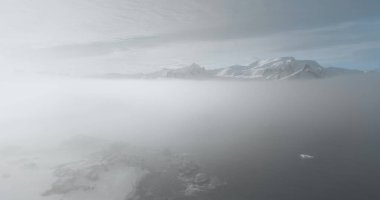 İnsansız hava aracı Antarktika okyanusu üzerinde sisli gökyüzü, karlı dağ zirveleri, arka planda gündoğumu bulutları. Antarktika sahilinde sabah sisi, sis bulutu. Hava manzaralı yüzey. Vahşi doğa arka planı