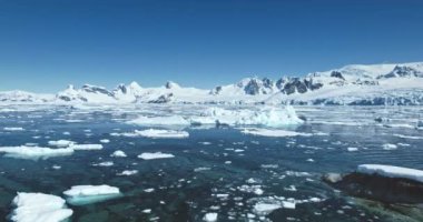 Güneşli Antarktika üzerinde uçmak, okyanus kayalık kıyıları, eriyen buzdağları, arka planda karla kaplı dağlar. Kutup görkemli vahşi deniz manzarası. Seyahat et, Antarktika 'yı keşfet. Düşük açılı İHA uçuşu