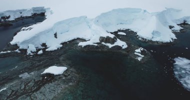 Antarktika kayalık kıyı şeridi hava manzarası. Soğuk kutup kıyısı koyunda su altında kayalar, buzul kaplı karlar. Antarktika gezisi keşfi. Ekoloji, eriyen buz, iklim değişikliği küresel ısınma