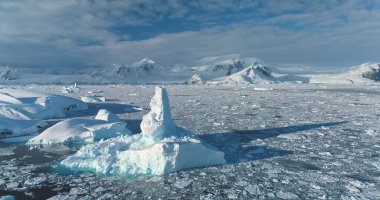 Mavi eriyen buzdağı yüzen okyanus suyu. Buz kütlesi Antarktika 'da mavi bulutlu gökyüzünün altında sürüklenir. Kar arka planda dağları kapladı. Ekoloji, eriyen buz, iklim değişikliği küresel ısınma