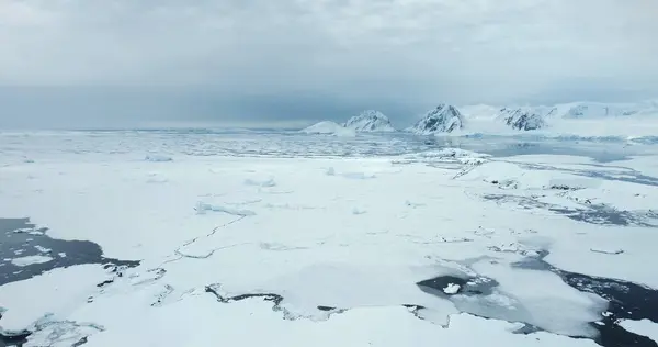 Frozen ocean Antarctica winter landscape aerial view. Cracked ice floes floating cold polar water, snow covered mountains in background. Discover the beauty of South Pole. Antarctic travel exploration