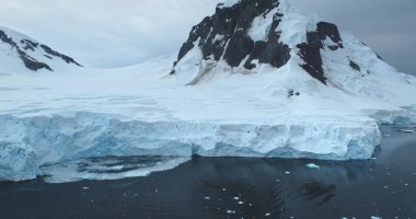 Muazzam mavi buzullar Antarktika 'nın kutup buzullarını kaplıyor. Dağlar karla kaplı kıyı şeridi. Ekoloji, eriyen buz, iklim değişikliği küresel ısınma. Antarktika vahşi doğa manzarasını keşfedin. İHA uçuşu
