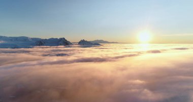 Drone flight over bright colorful clouds during sunset. Golden hour and amazing sun rays in blue sky. Beautiful ocean of fog at sunrise. Sun shines brightly over towering snow covered mountain range