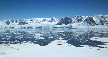 Amazing Antarctica winter landscape. Snow covered mountains towering polar ocean under bright blue sky. Ice floes icebergs melting in sunny day. Ecology, climate change, global warming. Aerial shot