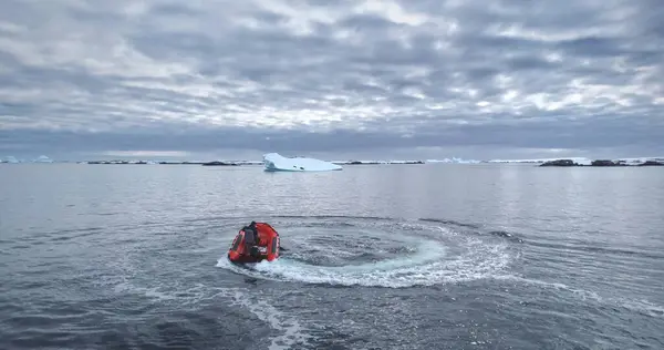 stock image Man riding zodiac boat make circle in water. Motorboat going around making white foam waves. Antarctica polar ocean coastline bay. Icebergs in background. People enjoy Antarctic travel and exploration