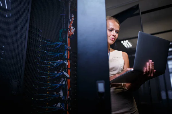 stock image IT engineer standing amid working server racks doing routine maintenance check and diagnostics using laptop computer (color toned image)