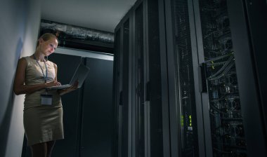 IT mühendisi, çalışan sunucuların arasında dizüstü bilgisayar kullanarak rutin bakım ve tanı kontrolü yapıyor (renk tonlu resim)
