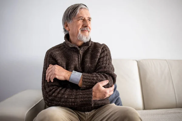 医療機器を使用して血圧を測定する高齢者 ソファの上に自宅に座って高血圧に苦しんでいる高齢者は彼の健康の世話をします — ストック写真