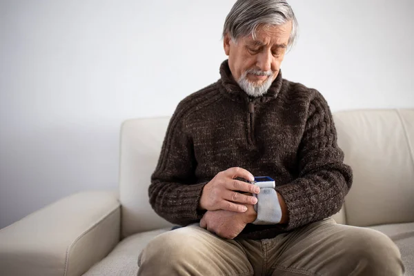 医療機器を使用して血圧を測定する高齢者 ソファの上に自宅に座って高血圧に苦しんでいる高齢者は彼の健康の世話をします — ストック写真