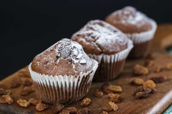 Fresh muffins with chocolate on a wooden board with dry grapes