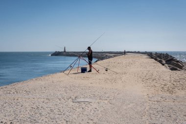 Figueira da Foz, Portugal - July 7, 2021: Man fishing on Atlantic Ocean coast in Figueira da Foz city, Coimbra District of Portugal clipart