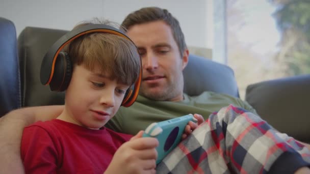 父亲带着儿子带着无线耳机在手持设备上玩电脑游戏 慢动作射击 — 图库视频影像