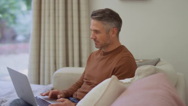 Ώριμος Άνδρας Στο Σπίτι Κάθεται Στον Καναπέ Χρησιμοποιώντας Φορητό Υπολογιστή — Αρχείο Βίντεο