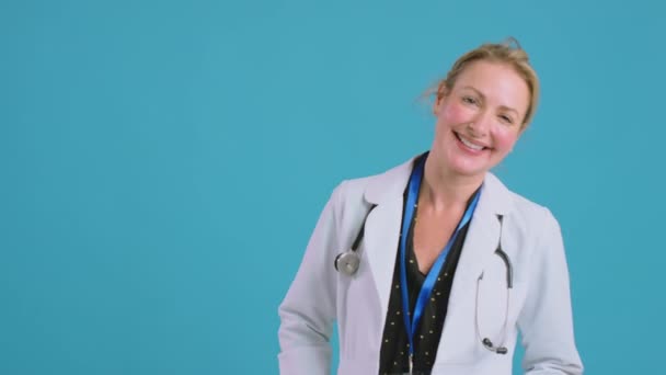 Mavi Stüdyonun Önünde Kameraya Bakan Beyaz Önlüklü Gülümseyen Kadın Doktor — Stok video
