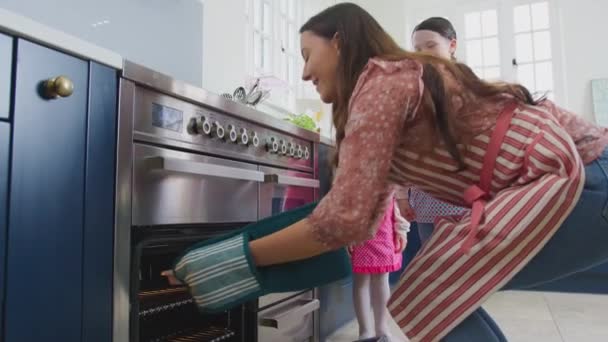 Äiti Kaksi Tytärtä Ottamassa Vastaleivottuja Leivoksia Uunista Keittiössä Kotona Ammuttu — kuvapankkivideo