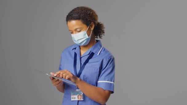 女护士身穿制服 戴口罩 带灰色背景数码平板的工作室肖像 慢镜头拍摄 — 图库视频影像