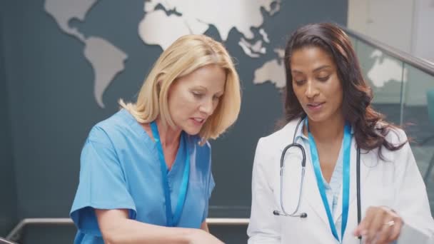 ホワイトコートとスクラブの2人の女性医師は 世界地図を背景に病院での非公式会議中に患者のメモを議論 スローモーションで撮影 — ストック動画