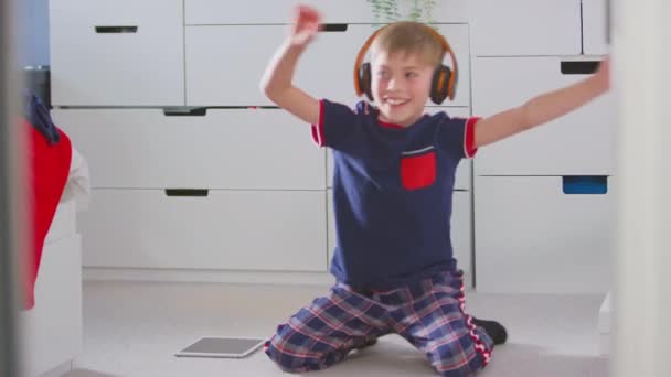 在卧室里的男孩 戴着无线耳机 坐在地板上听音乐 在数字平板电脑上跳舞 动作缓慢 — 图库视频影像