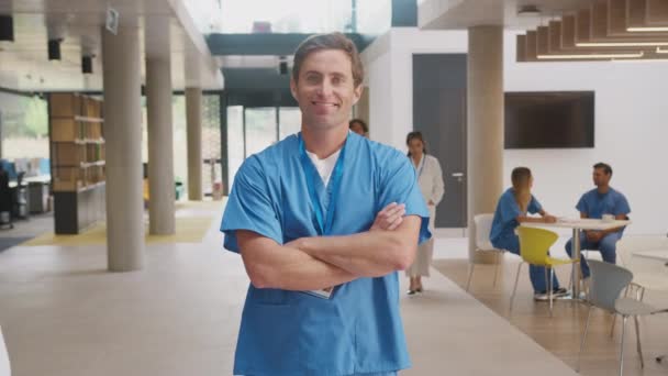 笑顔の男性医師の肖像画を身に着けているスクラブ立って 忙しい病院の建物で腕を折る スローモーションで撮影 — ストック動画