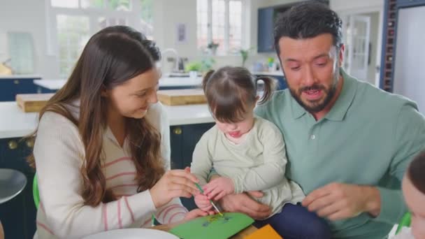 患有唐氏综合症的家庭的女儿坐在家里的桌子旁 用颜料和铅笔一起制作自制的贺卡 动作缓慢 — 图库视频影像