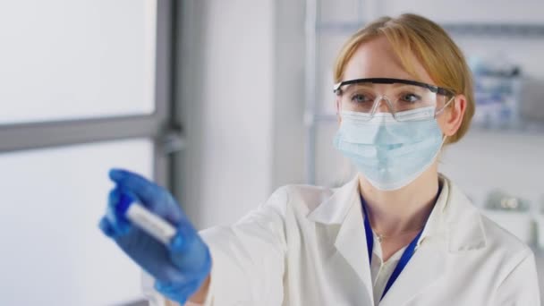 带着安全眼镜和面罩的女性实验室研究人员举着标有Omicron的试管 慢镜头相机的拉焦画像 — 图库视频影像