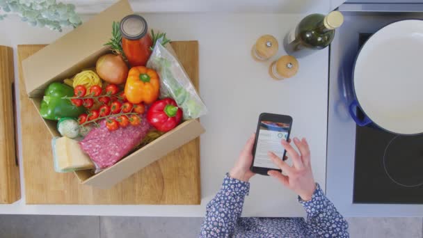 携帯電話でオンラインレシピを見て新鮮な食材とキッチンで女性のオーバーヘッドショット スローモーションで撮影 — ストック動画