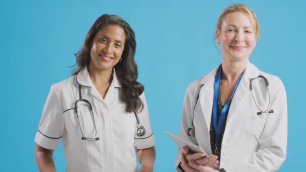 身穿白色外套 手持数码平板电脑 身穿制服的女医生面带微笑的画像 在蓝色摄影棚前对着镜头 慢镜头拍摄 — 图库视频影像
