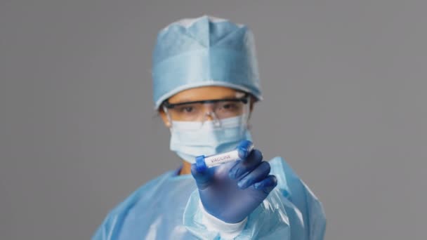 穿着Ppe的女性实验室工作人员和拿着标有 Quot 灰色背景疫苗 Quot 试管的安全眼镜的女性实验室工作人员的工作室肖像 — 图库视频影像