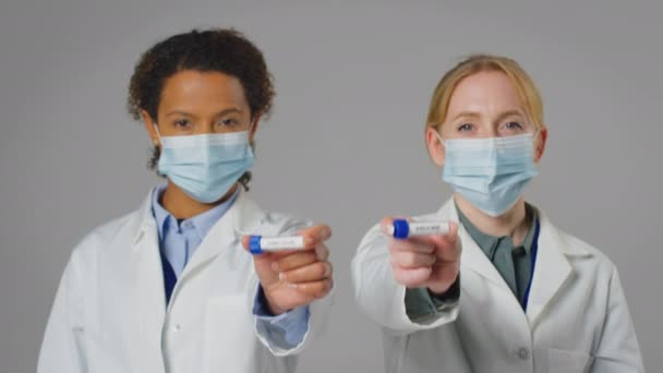 戴口罩的女性实验室研究人员手持标有Omicron和Vaccine的试管的演播室照片 慢动作拍摄 — 图库视频影像