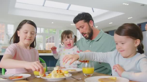 患有唐氏综合症的家庭女儿坐在桌旁 吃着煎饼 水果和糖浆当早餐 动作缓慢 — 图库视频影像