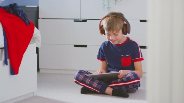 在卧室里的男孩 戴着无线耳机 坐在地板上玩数字平板电脑游戏 慢动作射击 — 图库视频影像