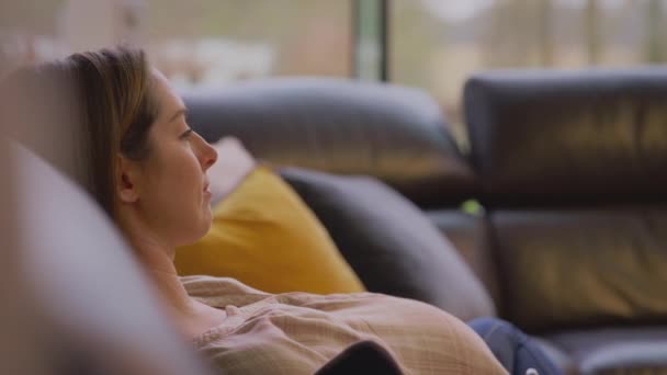 妊娠中の女性座っています上のソファにホーム見ますテレビ美しいですタッチバンプ ショットでスローモーション — ストック動画