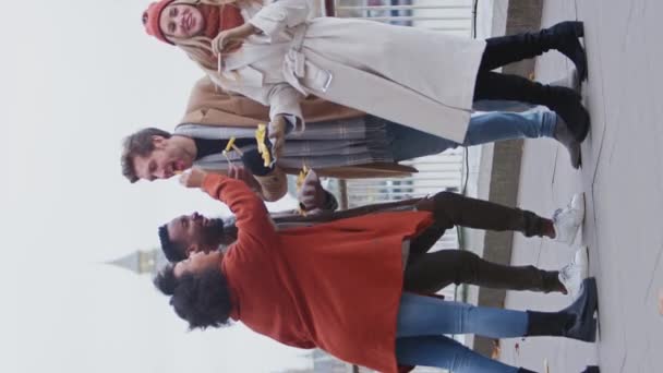 秋や冬のロンドン旅行で持ち帰りのフライドポテトを食べるコートやスカーフを身に着けている友人の垂直ビデオ スローモーションで撮影 — ストック動画