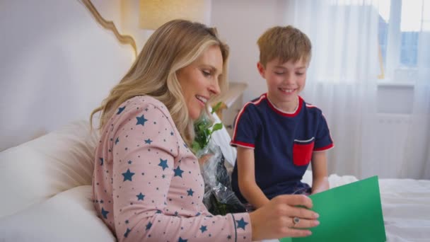 Liebender Sohn Überrascht Mutter Bett Mit Blumenstrauß Und Selbstgebastelter Karte — Stockvideo