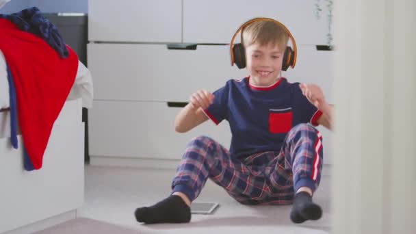 在卧室里的男孩 戴着无线耳机 坐在地板上听音乐 在数字平板电脑上跳舞 动作缓慢 — 图库视频影像