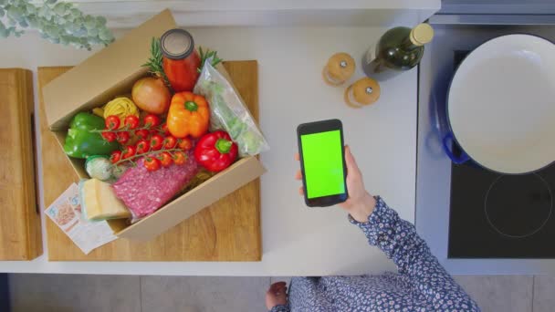 緑の画面の携帯電話でオンラインレシピを探している新鮮な食材をキッチンで女性のオーバーヘッドショット スローモーションで撮影 — ストック動画