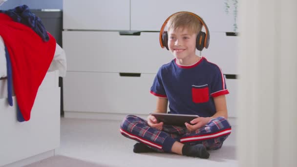 在卧室里的男孩 戴着无线耳机 坐在地板上听着数字平板电脑的音乐 动作缓慢 — 图库视频影像