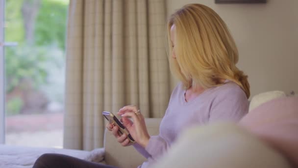 家中的成熟女人坐在沙发上 用手机拍摄 动作缓慢 — 图库视频影像