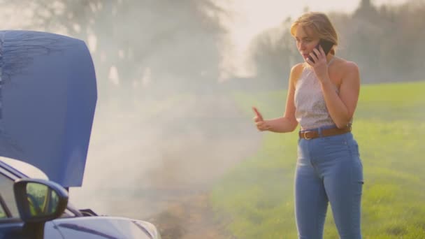 田舎道に立っている欲求不満な女性は ボンネットアップとエンジンから来る蒸気で車を分解し 携帯電話で助けを求める スローモーションで撮影 — ストック動画