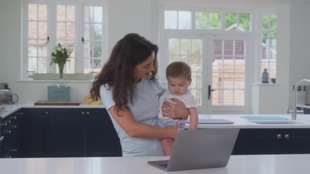 妈妈一边在家工作一边抱着小儿子 一边用笔记本电脑在厨房里慢动作地对接射击 — 图库视频影像