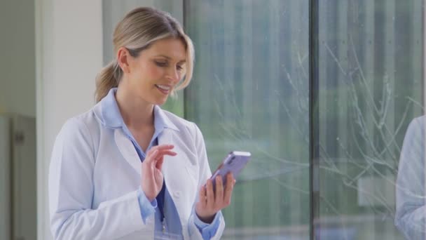 病院の廊下で携帯電話で話している白いコートを身に着けている女性医師 スローモーションで撮影 — ストック動画